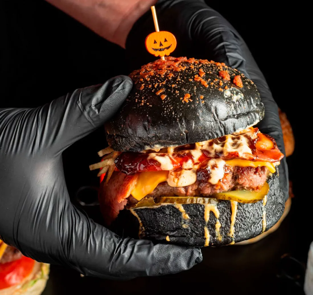 Burger de pan brioche negro sujetada con guante, de The Champions Burger